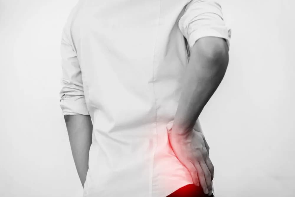 A person holding their lower back, with the painful area highlighted in red