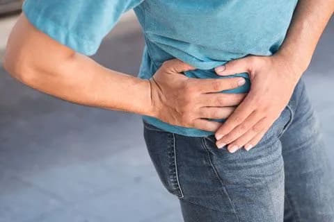 A man standing with both hands pressed to his painful hip