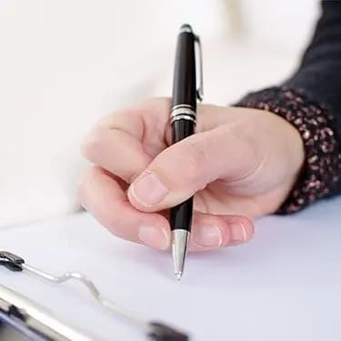 A hand holding a pen over a clipboard, filling in a form.