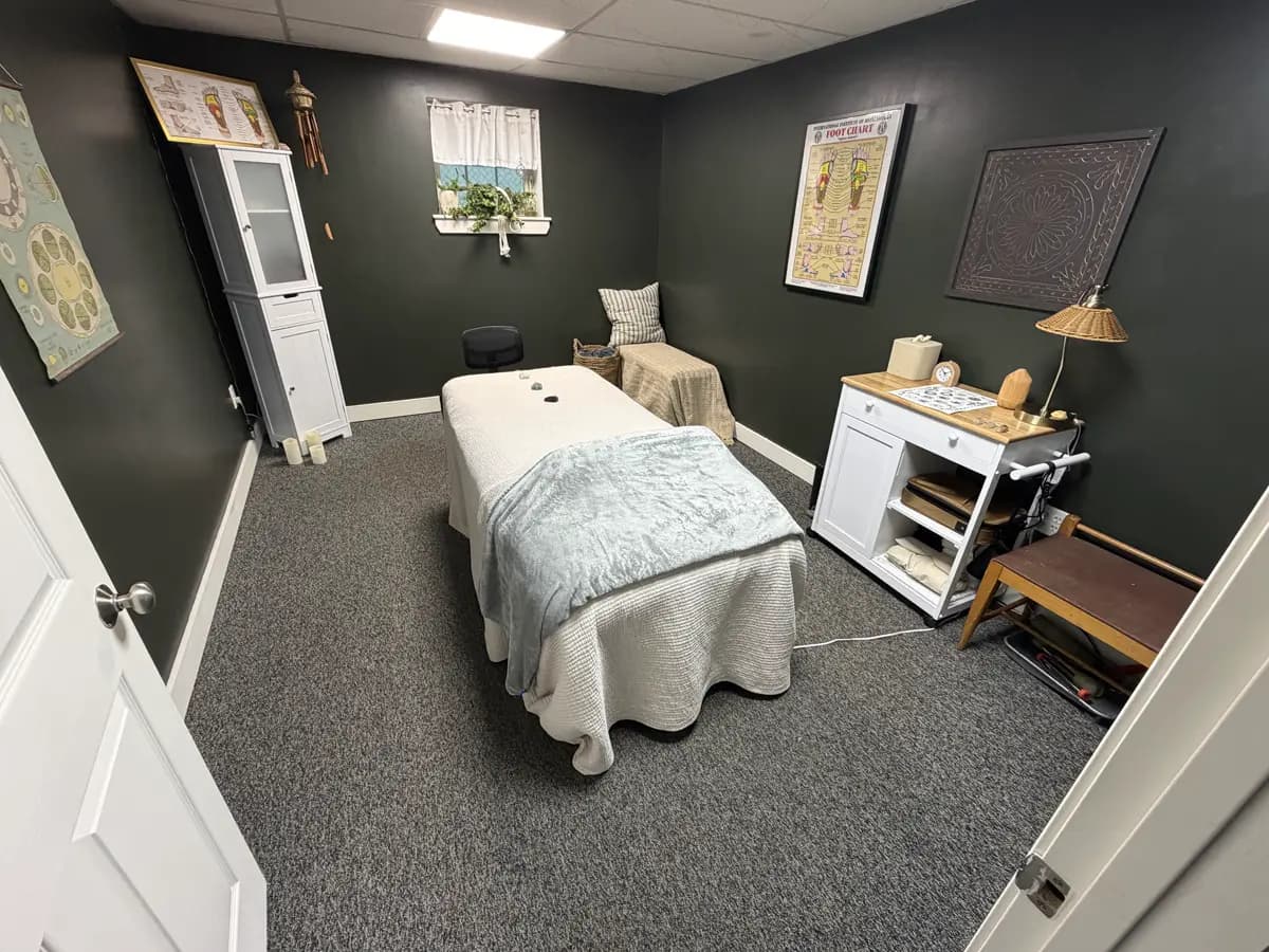 The massage room at Active Chiropractic: a made-up massage table under a soft blanket, dark green walls, a small window with a plant, and a side cart with towels