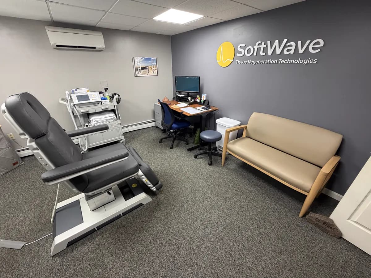 The SoftWave room: a treatment chair, the SoftWave unit on its cart and a sofa, with the SoftWave logo on the wall.