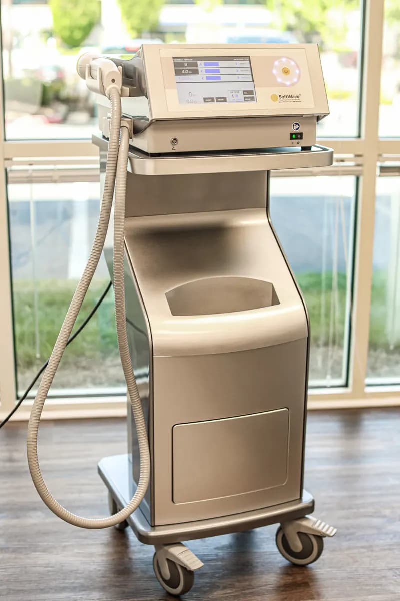 The SoftWave device: a touchscreen control unit on a wheeled cart, with the handheld applicator on a cable at its side