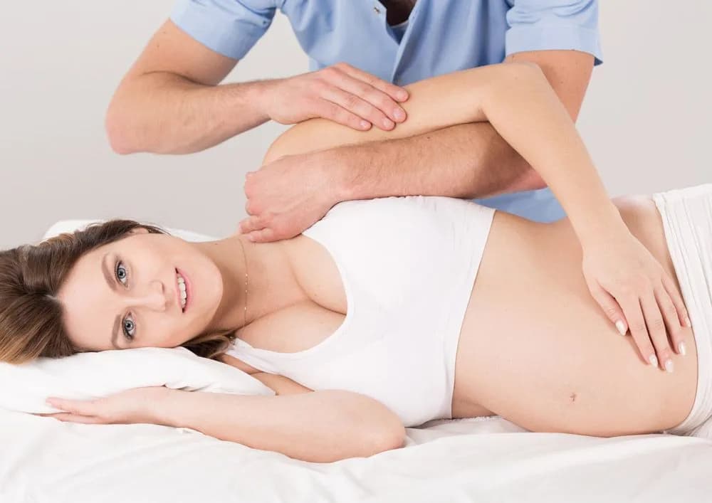 A pregnant woman lying on her side on a treatment table while a chiropractor works on her spine