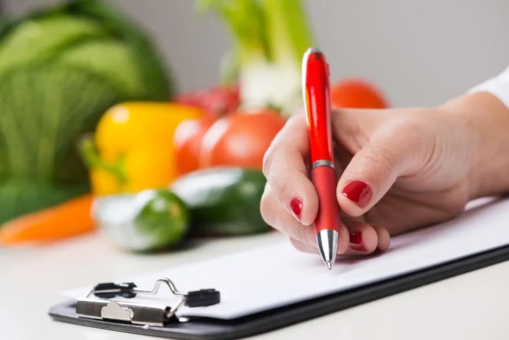 Writing an eating plan on a clipboard beside fresh vegetables